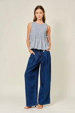 Load image into Gallery viewer, Woman wearing a sleeveless checkered top and wide-leg jeans on a plain background
