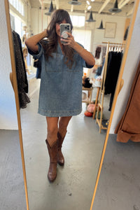 Person wearing a denim dress and brown boots in a clothing store.