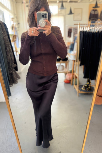 Person taking a mirror selfie wearing a brown cardigan and dark pants in a clothing store.