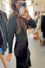 Load image into Gallery viewer, Person wearing a green long-sleeve top and black pants in a clothing store.