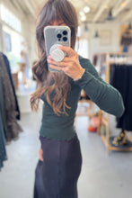 Load image into Gallery viewer, Person taking a mirror selfie wearing a green top and dark pants in a store setting.