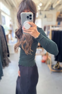 Person taking a mirror selfie wearing a green top and dark pants in a store setting.