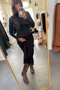 Person taking a mirror selfie wearing a black top and brown pants in a clothing store.