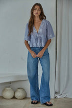 Load image into Gallery viewer, Woman wearing a blue patterned top and jeans standing indoors.