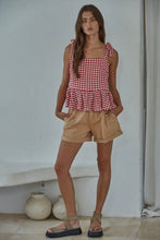 Load image into Gallery viewer, Woman wearing a red and white checkered top and beige shorts against a plain wall.