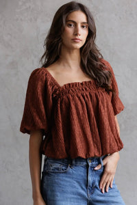 Woman wearing a brown textured top and blue jeans against a gray background