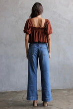 Load image into Gallery viewer, Woman wearing a brown top and blue jeans standing against a gray wall.