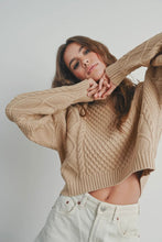 Load image into Gallery viewer, Woman wearing a beige cable knit sweater and light-colored pants against a plain background
