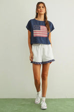 Load image into Gallery viewer, Woman wearing a denim shirt with an American flag design and white shorts on a plain background