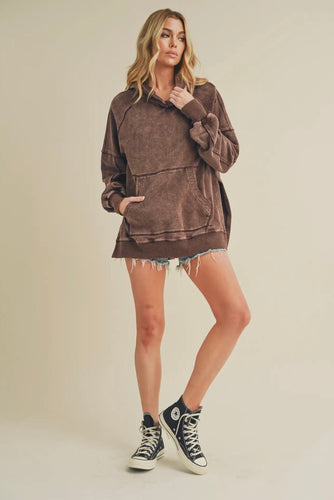 Woman wearing a brown oversized hoodie and black high-top sneakers on a beige background
