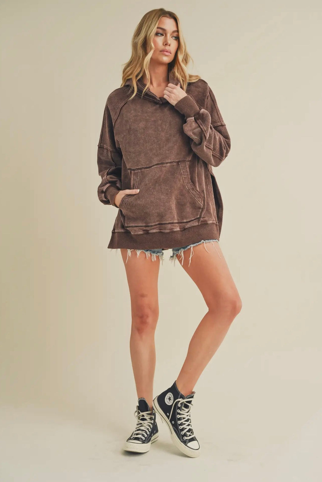 Woman wearing a brown oversized hoodie and black high-top sneakers on a beige background