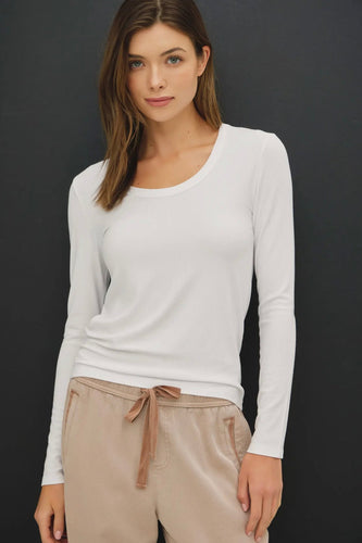Woman wearing a white long-sleeve top and beige pants against a dark background