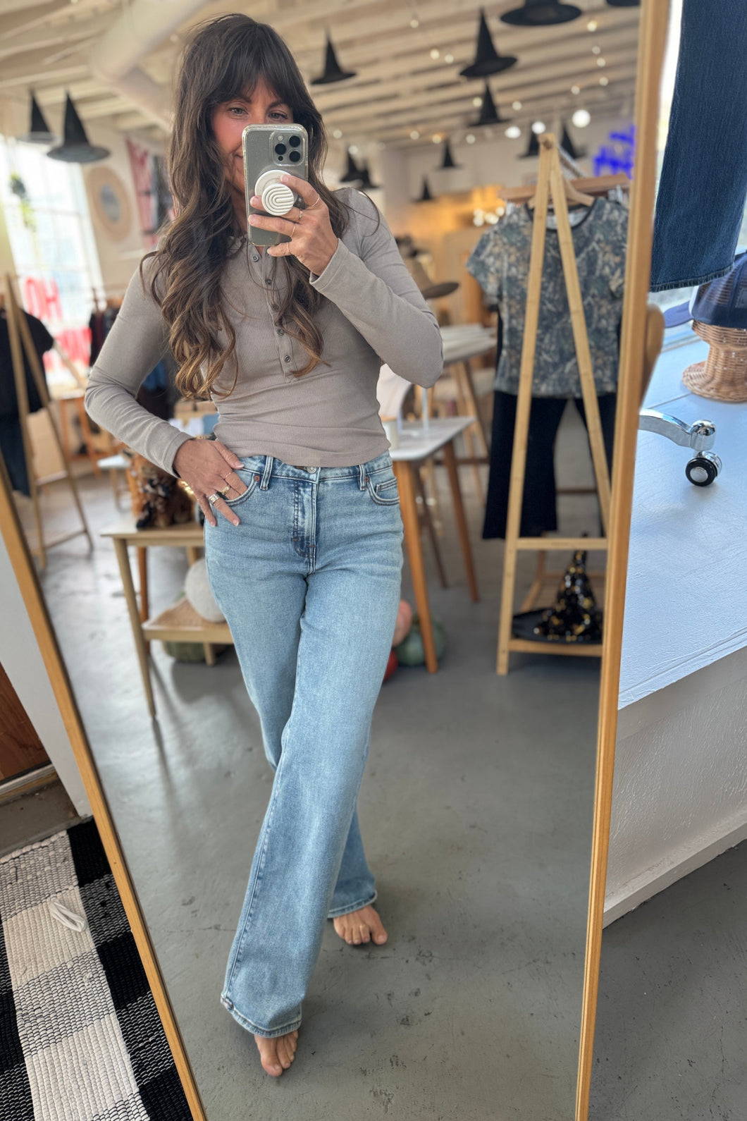 Woman taking a mirror selfie wearing a beige top and light blue jeans in a store.