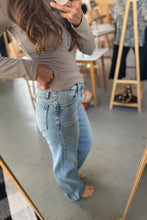 Load image into Gallery viewer, Person wearing light blue jeans standing in a room with wooden furniture and a coat rack.