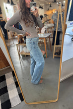 Load image into Gallery viewer, Person taking a mirror selfie wearing a beige long-sleeve top and light blue jeans in a store setting.