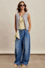 Load image into Gallery viewer, Woman wearing a sleeveless vest, yellow top, blue jeans, and sunglasses against a beige background