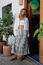 Load image into Gallery viewer, Woman in a layered skirt and jacket standing in front of a door with plants around.