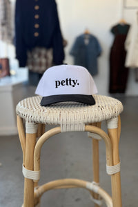 White cap with 'petty.' text on a wicker stool in a clothing store setting