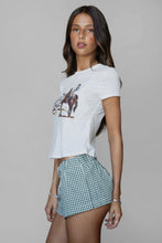 Load image into Gallery viewer, Woman wearing a white t-shirt with a graphic design and a checkered skirt on a plain background