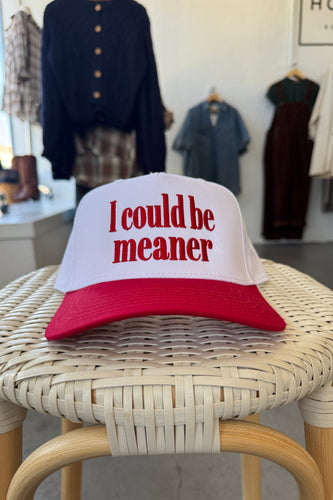 Cap with text 'I could be meaner' on a wicker chair with clothing in the background