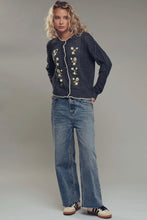 Load image into Gallery viewer, Woman wearing a dark blue knitted cardigan with floral patterns and blue jeans on a plain background