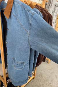 Stack of blue jeans on a wooden rack with other clothing items in the background.