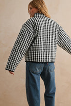 Load image into Gallery viewer, Person wearing a black and white checkered shirt and blue jeans against a beige background