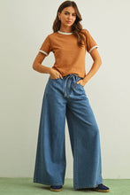 Load image into Gallery viewer, Woman wearing a brown top and blue jeans against a plain background