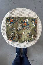 Load image into Gallery viewer, Decorative mat with floral pattern on a woven circular frame, on a concrete floor.