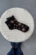 Load image into Gallery viewer, Black sock with floral pattern on a woven stool