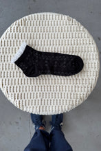 Load image into Gallery viewer, Black sock with white polka dots on a textured stool, person wearing blue jeans and shoes in the background.
