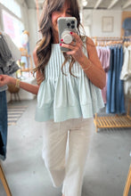 Load image into Gallery viewer, Woman taking a mirror selfie wearing a light green pleated top and beige pants in a clothing store.