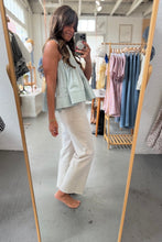 Load image into Gallery viewer, Woman taking a mirror selfie in a clothing store wearing a light green top and white pants.