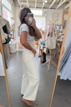 Load image into Gallery viewer, Person taking a mirror selfie wearing a striped shirt and white pants in a store.