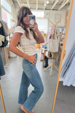 Load image into Gallery viewer, Woman taking a mirror selfie in a clothing store wearing a white top and blue jeans.