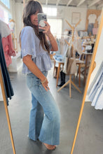 Load image into Gallery viewer, Woman taking a mirror selfie wearing a light blue top and jeans in a clothing store.