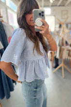 Load image into Gallery viewer, Woman taking a mirror selfie wearing a light blue top and jeans in a clothing store.