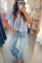 Load image into Gallery viewer, Woman taking a mirror selfie wearing a light blue blouse and jeans in a clothing store.