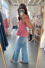 Load image into Gallery viewer, Woman taking a mirror selfie wearing a red checkered top and blue jeans in a clothing store.
