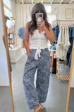 Load image into Gallery viewer, Woman taking a mirror selfie wearing a white top and blue floral pants in a clothing store.