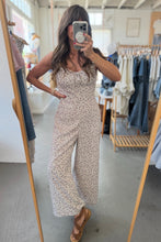 Load image into Gallery viewer, Woman taking a mirror selfie wearing a floral jumpsuit in a clothing store.