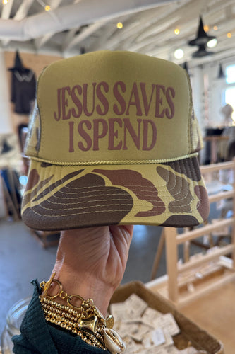 Hand holding a pouch with 'Jesus Saves I Spend' text in a blurred indoor setting