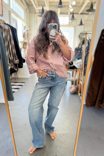 Person taking a mirror selfie wearing a striped shirt and jeans in a clothing store.