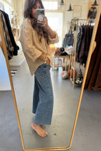 Load image into Gallery viewer, Person taking a mirror selfie wearing a beige sweater and blue jeans in a clothing store.