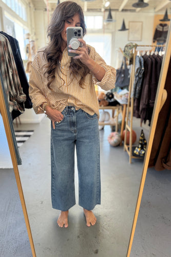 Person taking a mirror selfie wearing a striped shirt and jeans in a clothing store.