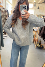 Load image into Gallery viewer, Person wearing a gray sweater and light blue jeans taking a mirror selfie in a clothing store.