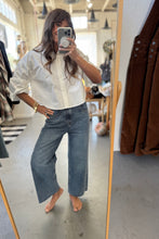Load image into Gallery viewer, Person taking a mirror selfie wearing a white shirt and blue jeans in a store.