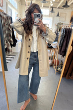 Load image into Gallery viewer, Person taking a mirror selfie wearing a beige trench coat, white shirt, and blue jeans in a clothing store.