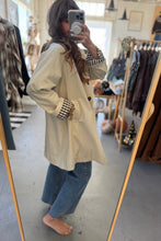 Load image into Gallery viewer, Person wearing a beige trench coat and blue jeans in a clothing store.