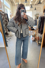Load image into Gallery viewer, Person wearing a black and white checkered shirt and blue jeans in a clothing store.